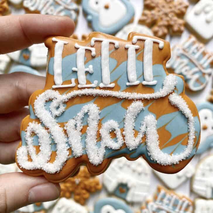 photo of writing with royal icing on a cookie: pressure piped saying LET IT SNOW