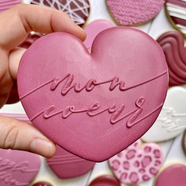 photo of cookie decorated with royal icing using month glade font saying MON COEUR