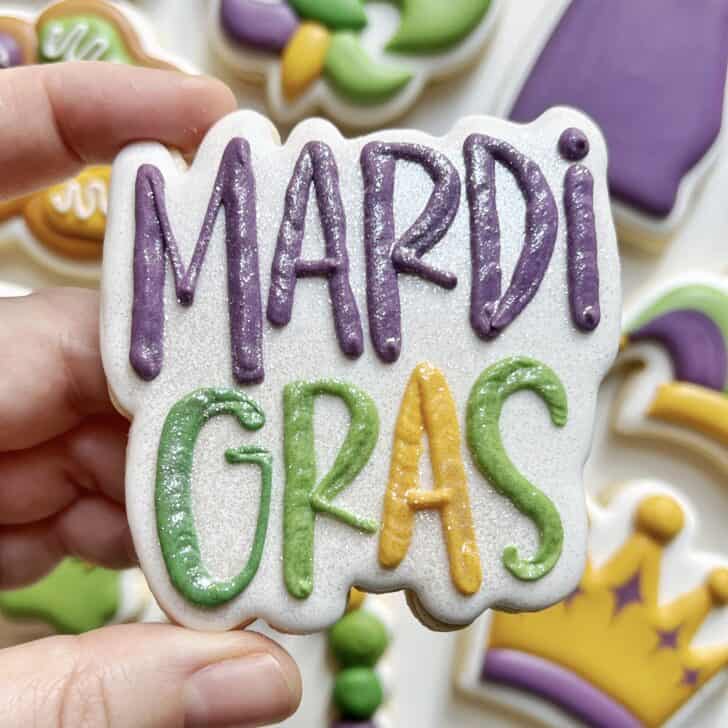 photo of writing with royal icing on a cookie: pressure piped saying MARDI GRAS