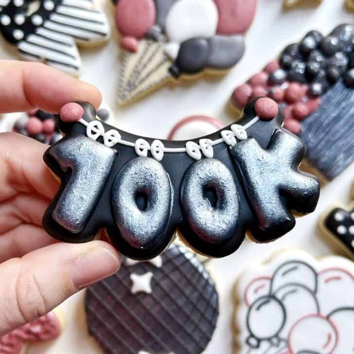 photo of writing with royal icing on a cookie: pressure piped saying 100K