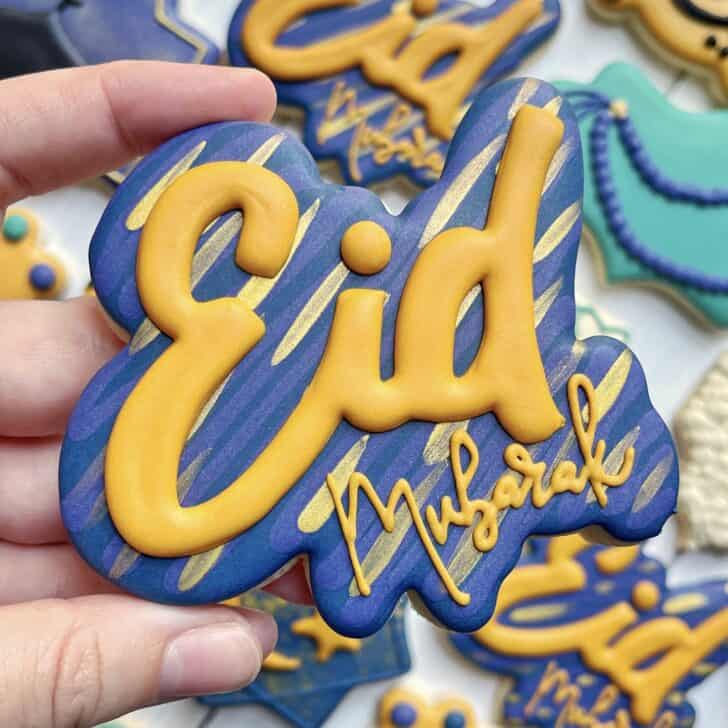 photo of writing with royal icing on a cookie: pressure piped saying EID MUBARAK