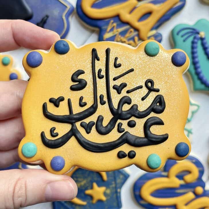 photo of writing with royal icing on a cookie: pressure piped saying EID MUBARAK in Arabic