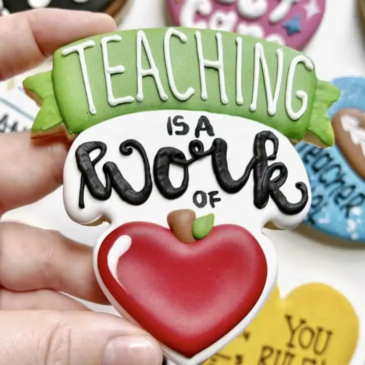 photo of writing with royal icing on a cookie: pressure piped saying TEACHING IS A WORK OF HEART