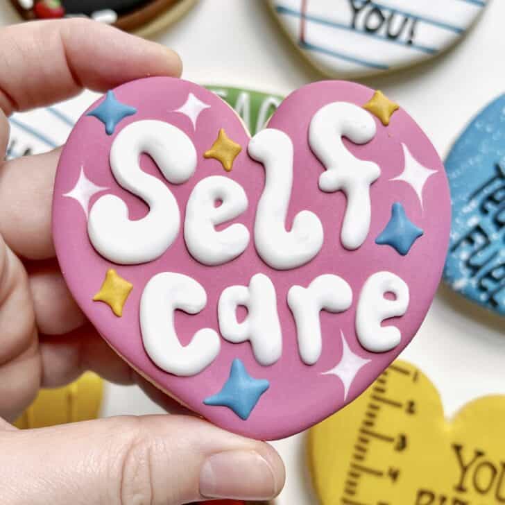photo of writing with royal icing on a cookie: pressure piped saying SELF CARE