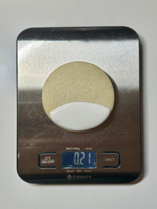 image of cookie partially flooded on a piece of paper on top of a food scale to measure royal icing amount