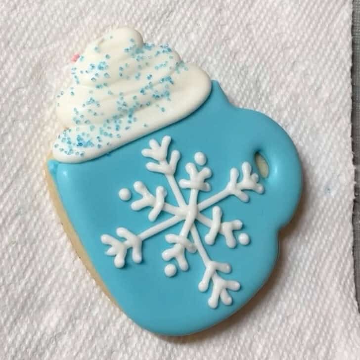 Step-by-step decorating instructions for how to decorate snowflake mug cookies with royal icing
