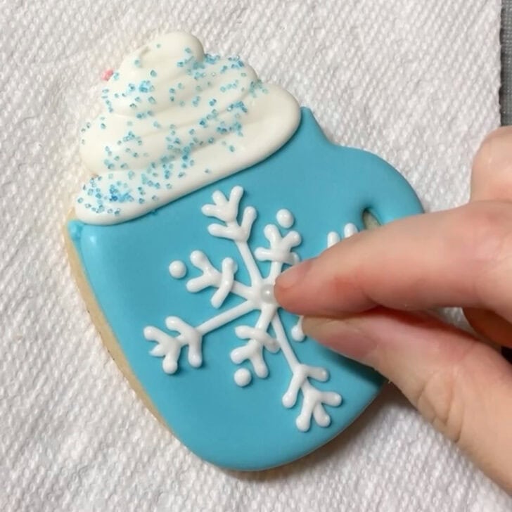 Step-by-step decorating instructions for how to decorate snowflake mug cookies with royal icing