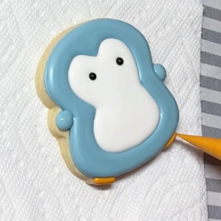 Step-by-step decorating instructions for how to decorate penguin sugar cookies with realizing