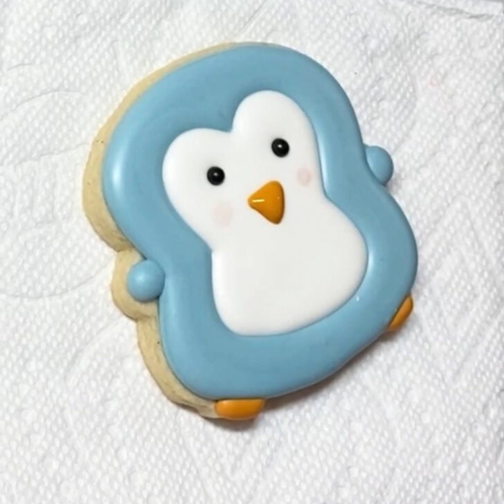 Step-by-step decorating instructions for how to decorate penguin sugar cookies with realizing