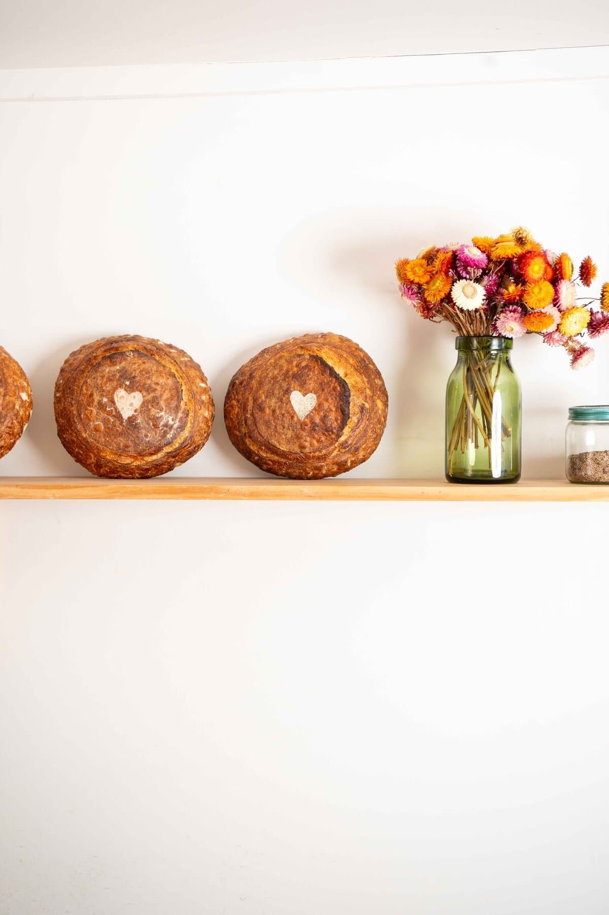 Heart-shaped sourdough breads on a shelf with a flower vase and jar.