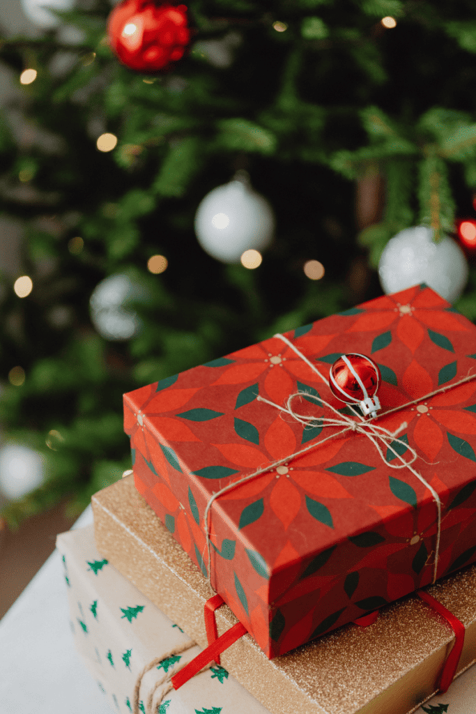 Five Ways to Spend Less Money This Holiday Season. Presents with tree in background.
