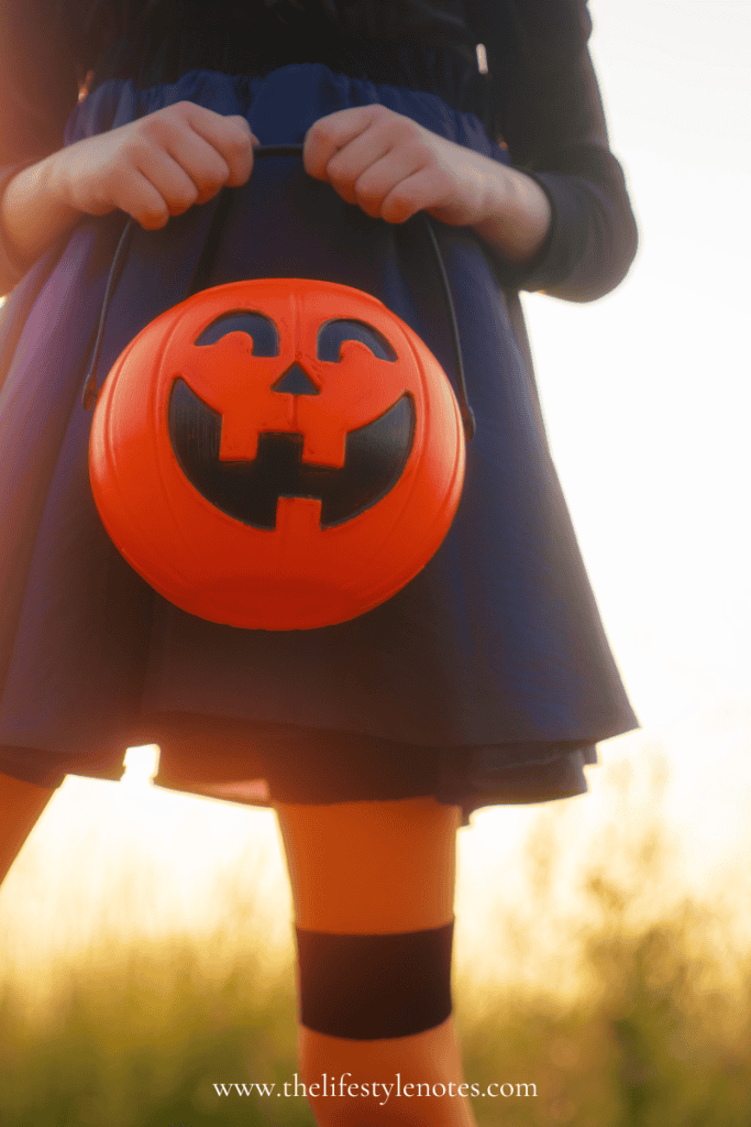 How to Have a Budget-Friendly Halloween. Little girl in orange and black holding a pumpkin bucket.