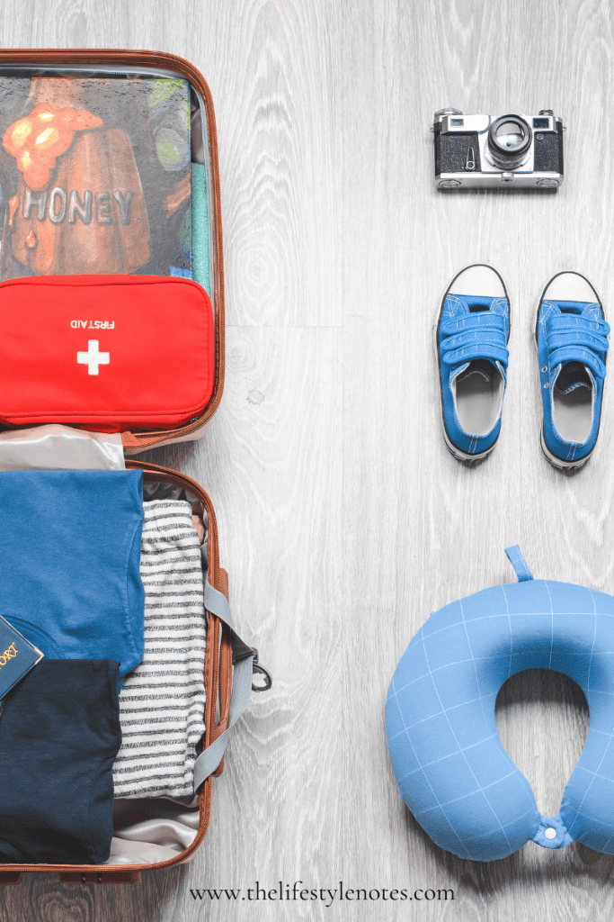 Tips for a Stress-Free Trip. Child's suitcase open with clothes, passport, first aid kit. Next to suitcase are sneakers, neck pillow and camera.