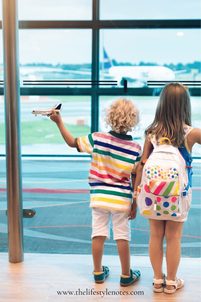 Two kids standing at a window in an airport, watching planes outside.
