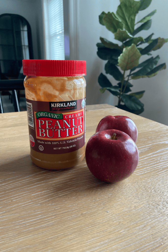 Jar of peanut butter and two apples on table.