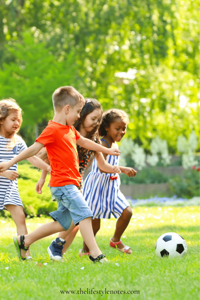 Four young kids running outside on the grass with a soccer bal