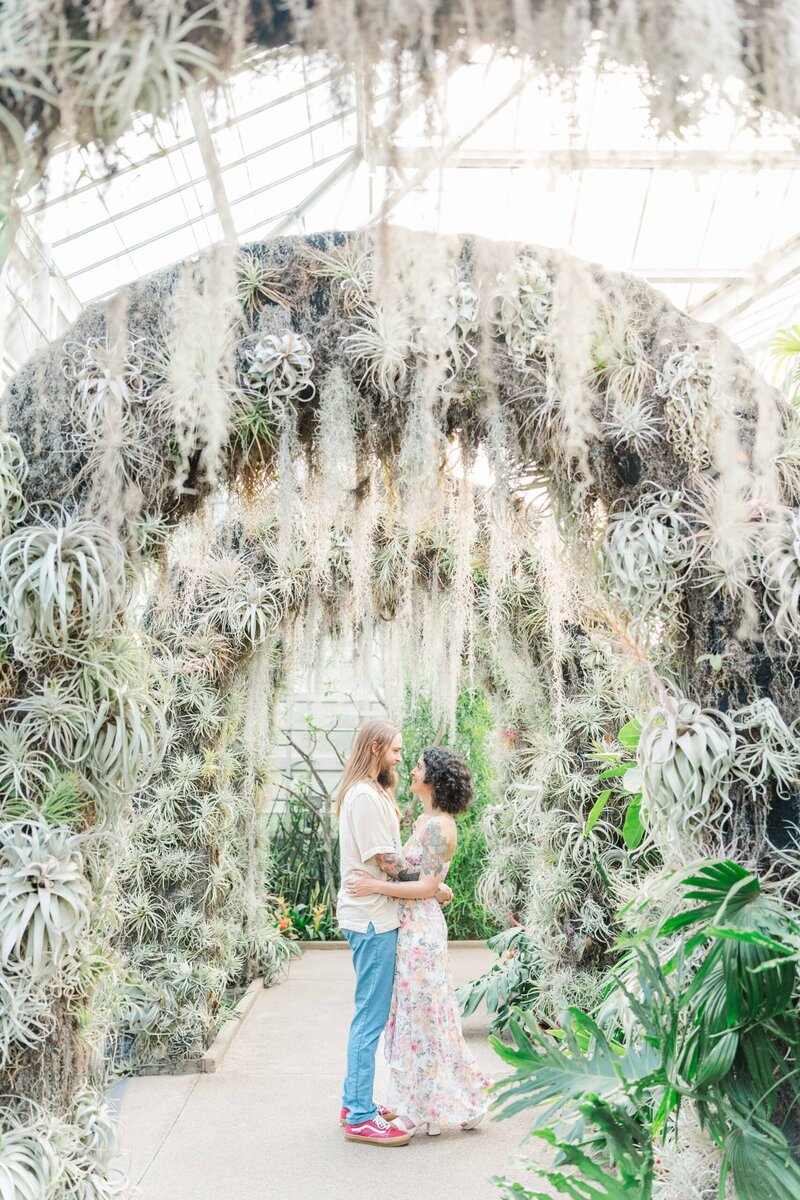 Future bride and groom standing under archway of succulents and air plants