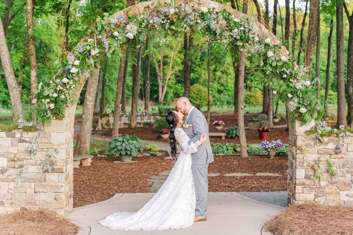bride and groom kissing under the flower arch