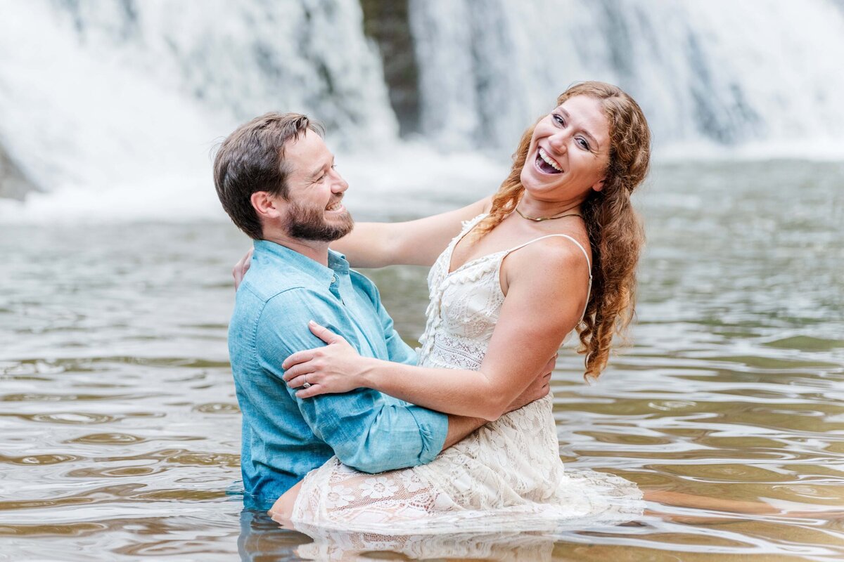 Couple splashing at the base of McGalliard Falls waterfall engagement session Valdese NC
