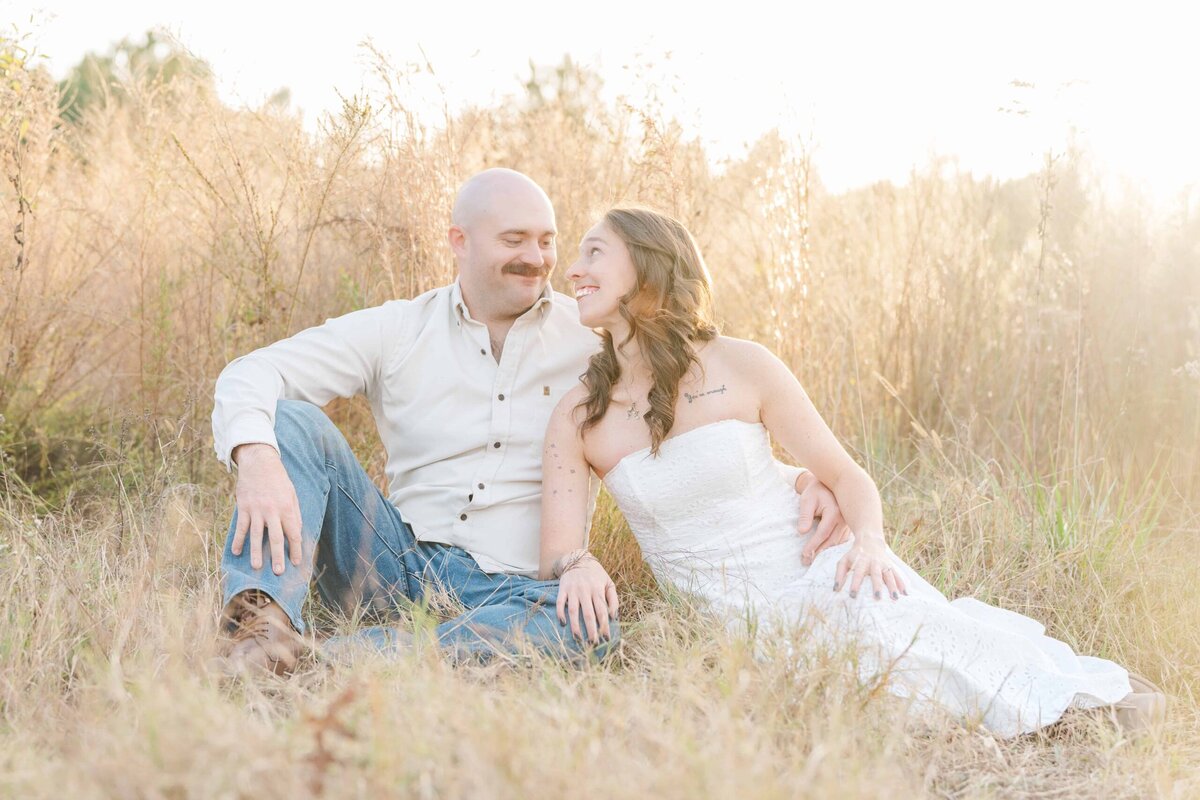Outdoor engagement photos Charlotte couple sitting in golden grass at sunset