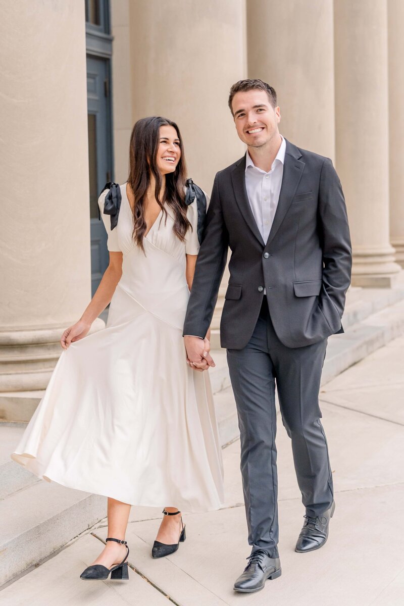 Engaged couple walking in front of elegant white columns in Uptown Charlotte