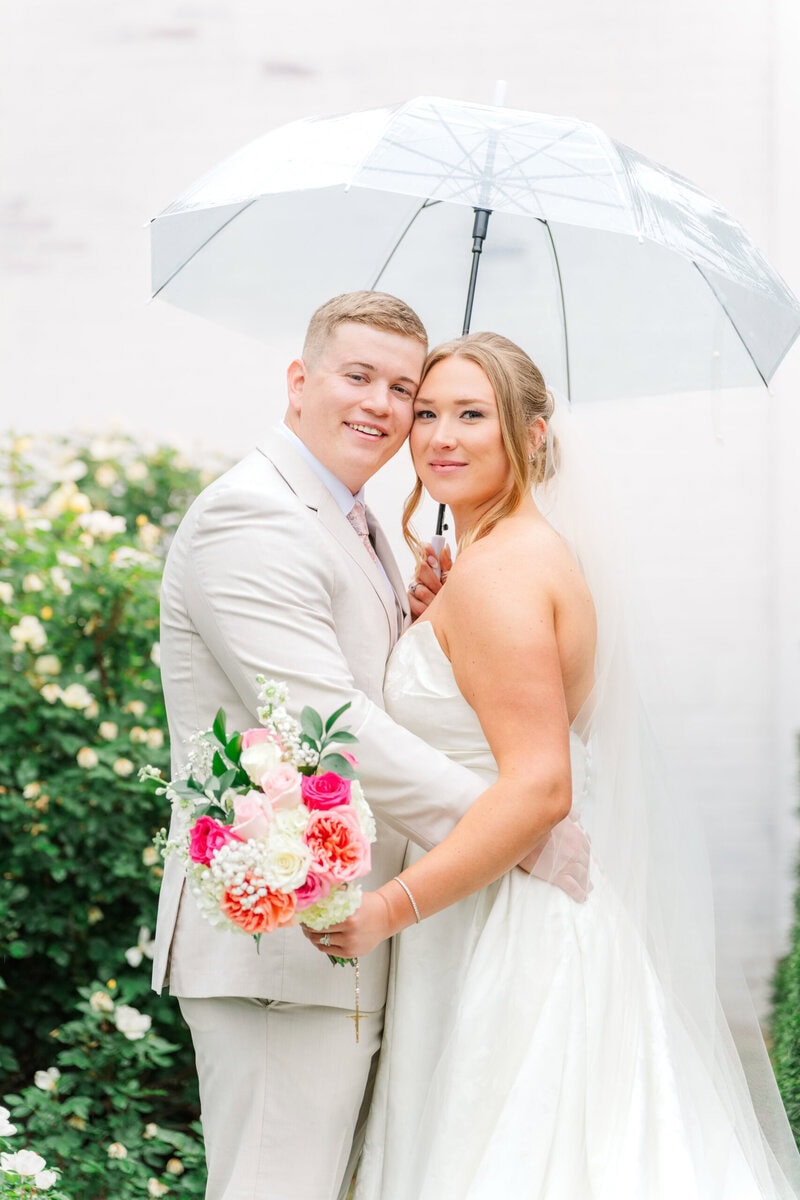 bride and groom holding umbrella in rain outside Mariposa Chapel little white chapel near Charlotte