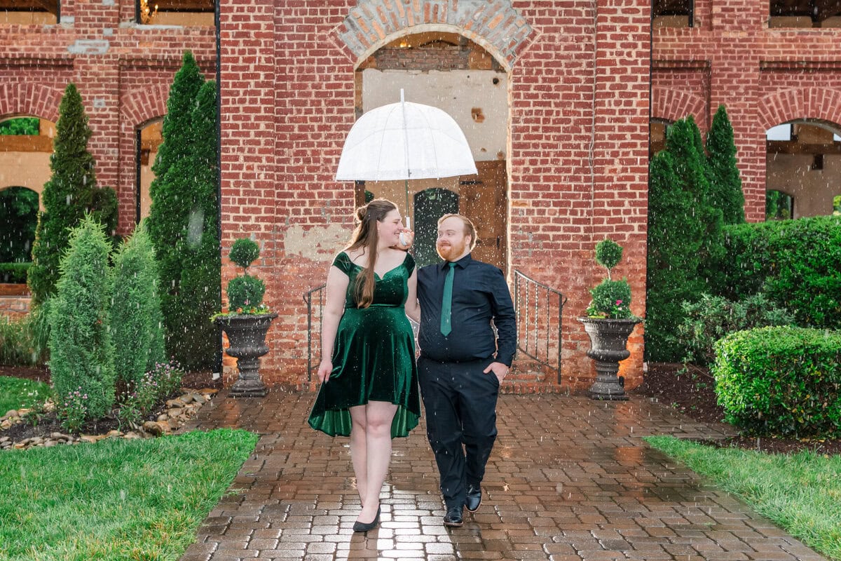 Couple sharing a clear umbrella during rainy engagement session at The Providence Cotton Mill in Maiden NC
