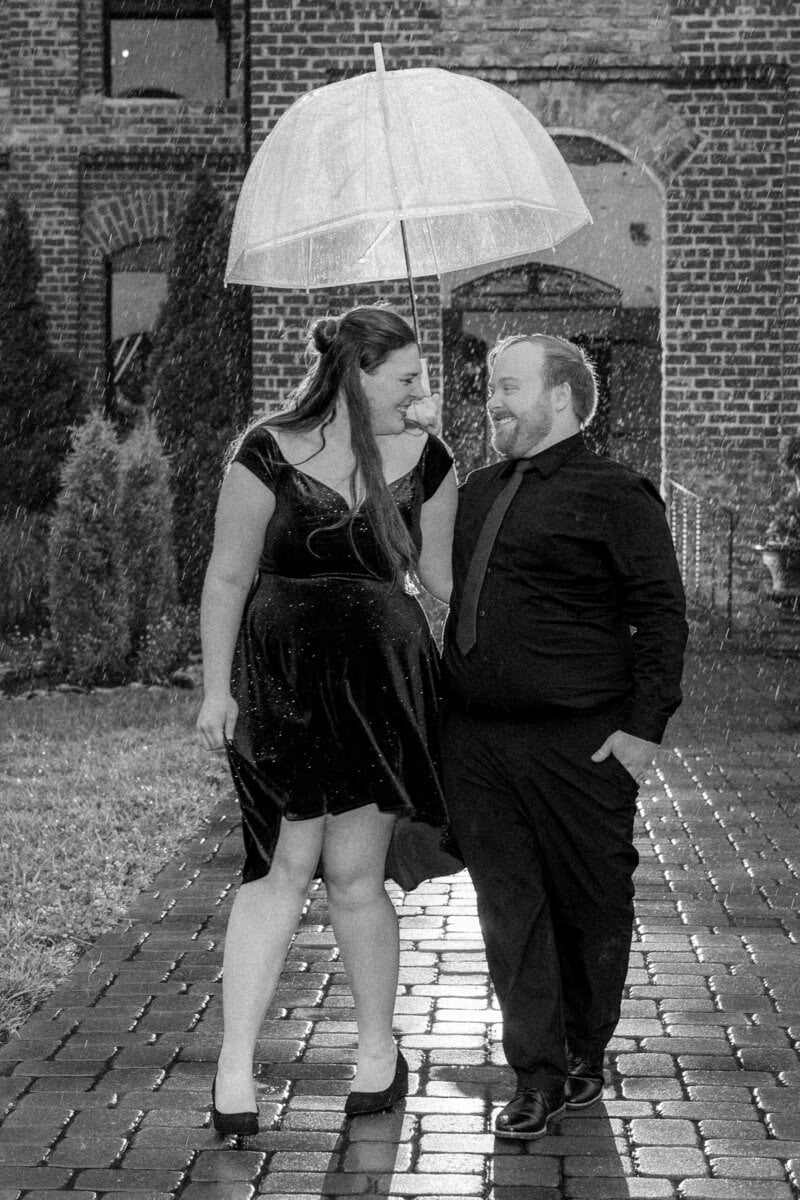 Groom laughing with bride under clear umbrella at rainy North Carolina engagement session