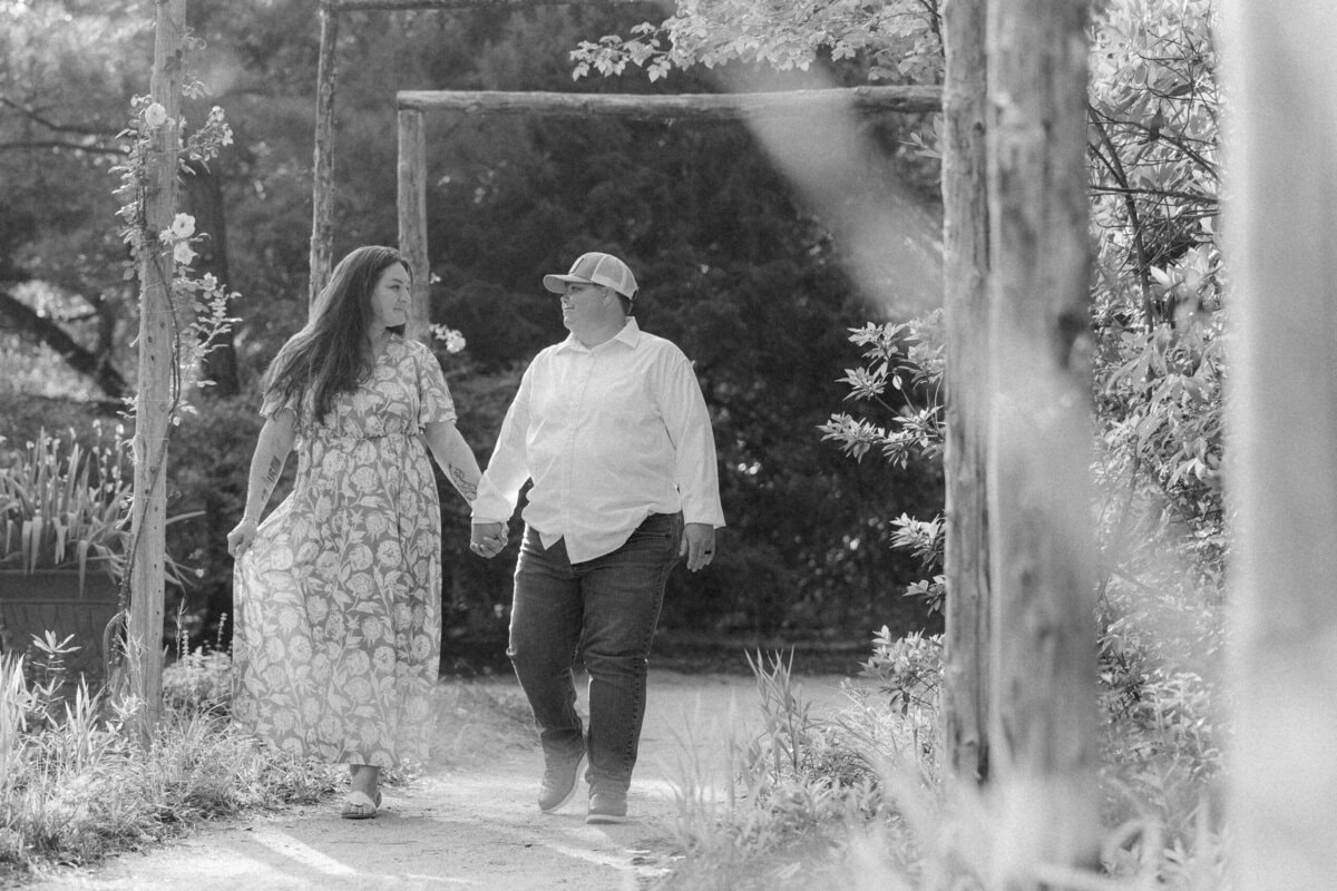 Same-sex couple walking hand in hand along the path toward the pond at Kamila Gardens