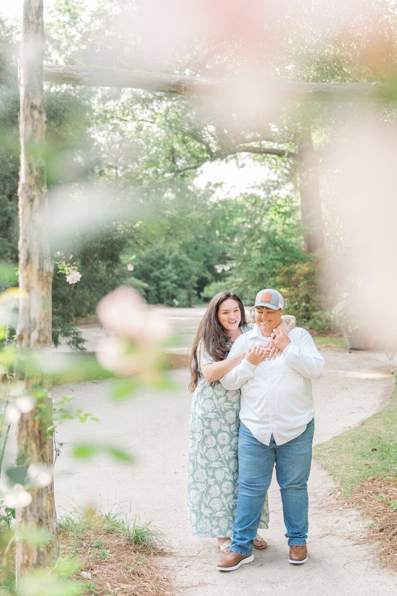 Nikki and Ashley laughing together near the entrance gates at Kamila Gardens, LGBTQ+ engagement photos North Carolina