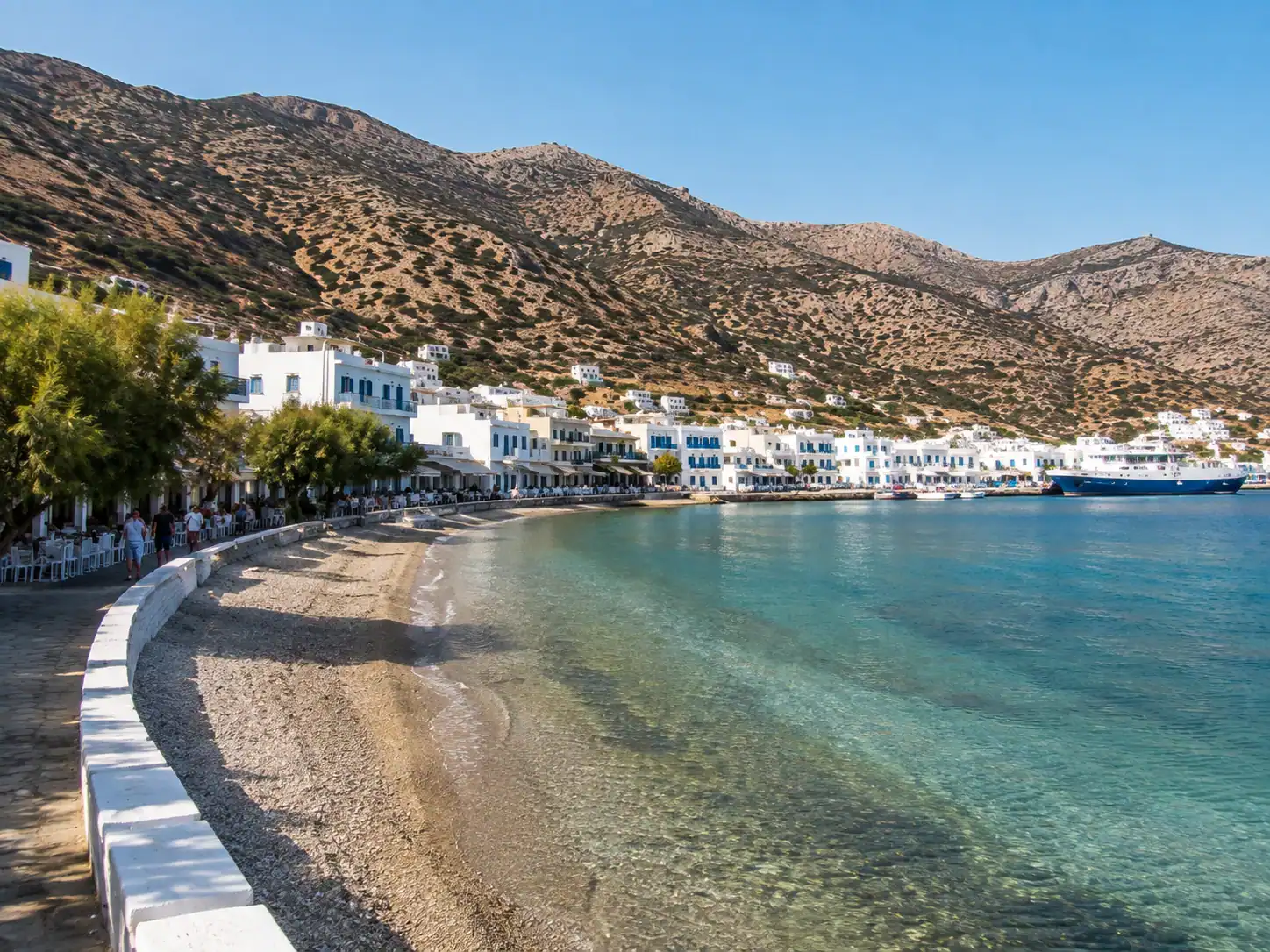 Kamares bay in Sifnos with whitewashed waterfront buildings, sandy beach and ferry harbor beneath Cycladic hills