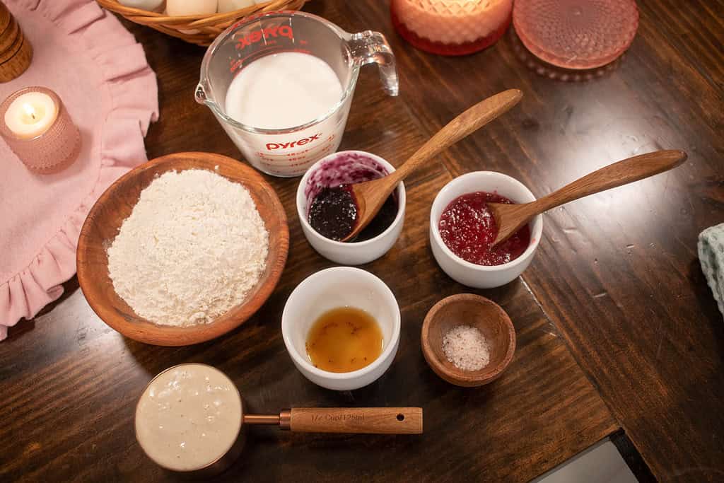 ingredients for sourdough raspberry popovers in wooden and white glass bowls on a wooden countertop in a cottage kitchen
