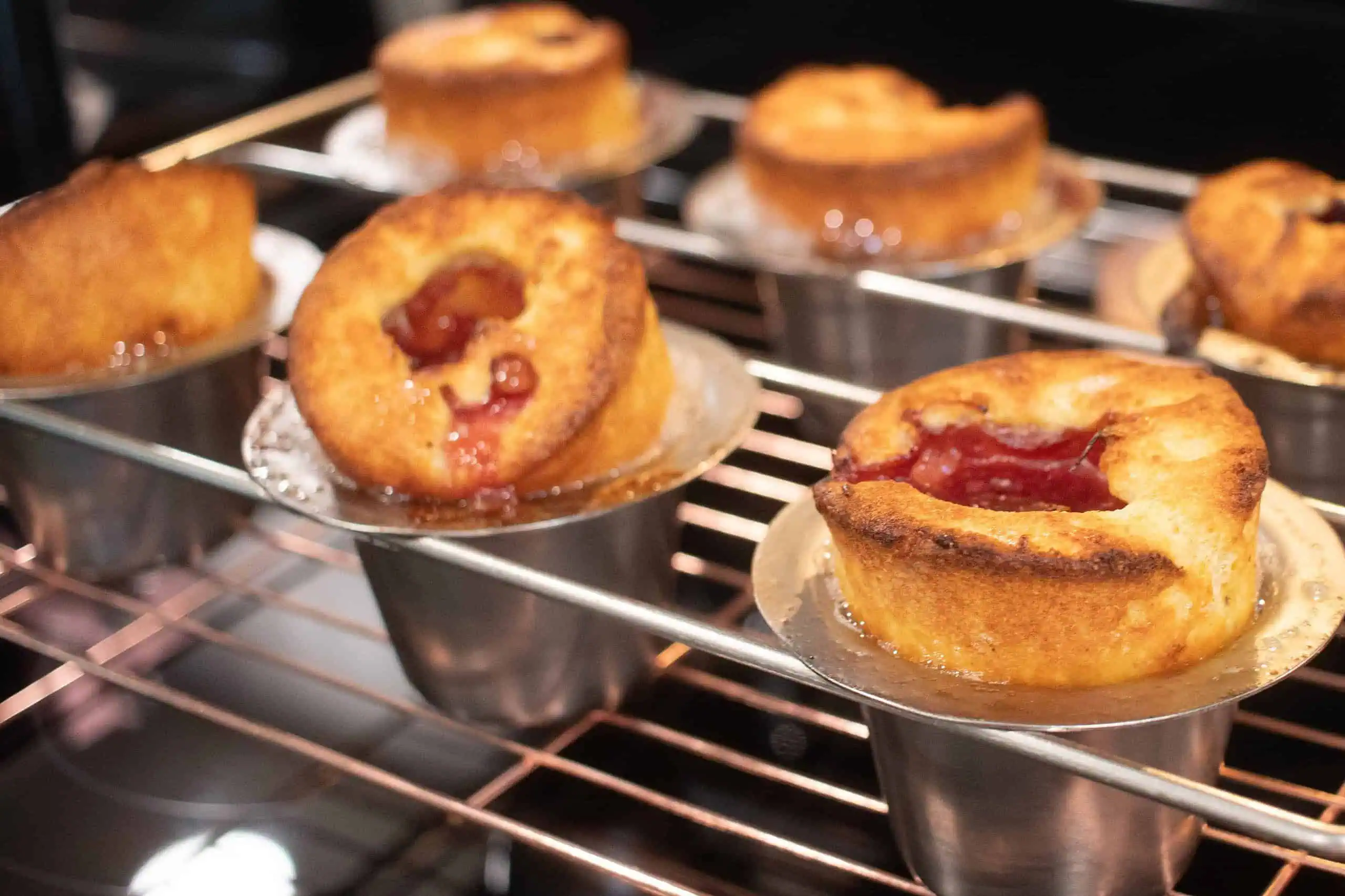 a close up of sourdough raspberry popovers in a silver popover pan on a wire rack