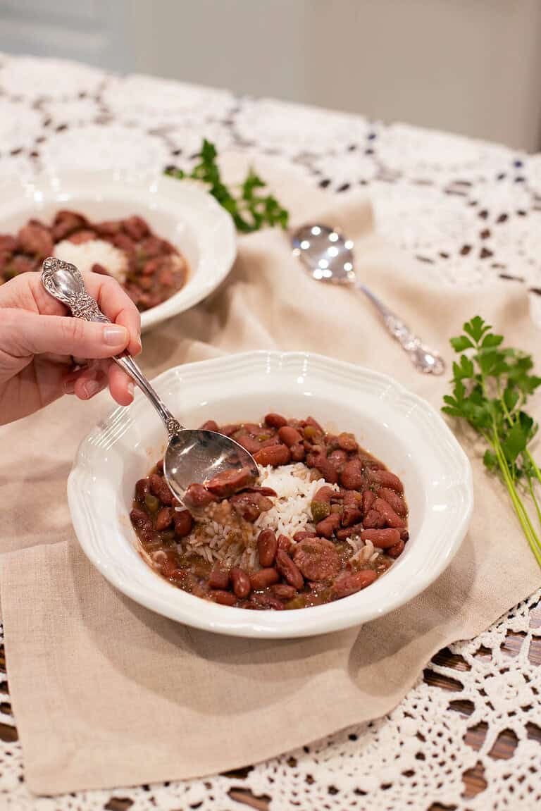 A hand scooping a spoonful of red beans and rice from a bowl, showing the rich, hearty texture of the dish.