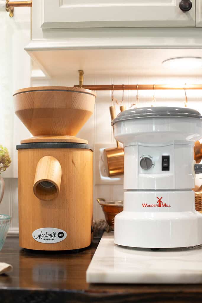 A Mockmill Professional 200 grain mill and a WonderMill electric grain mill side-by-side on a kitchen counter, showing options for milling flour at home.