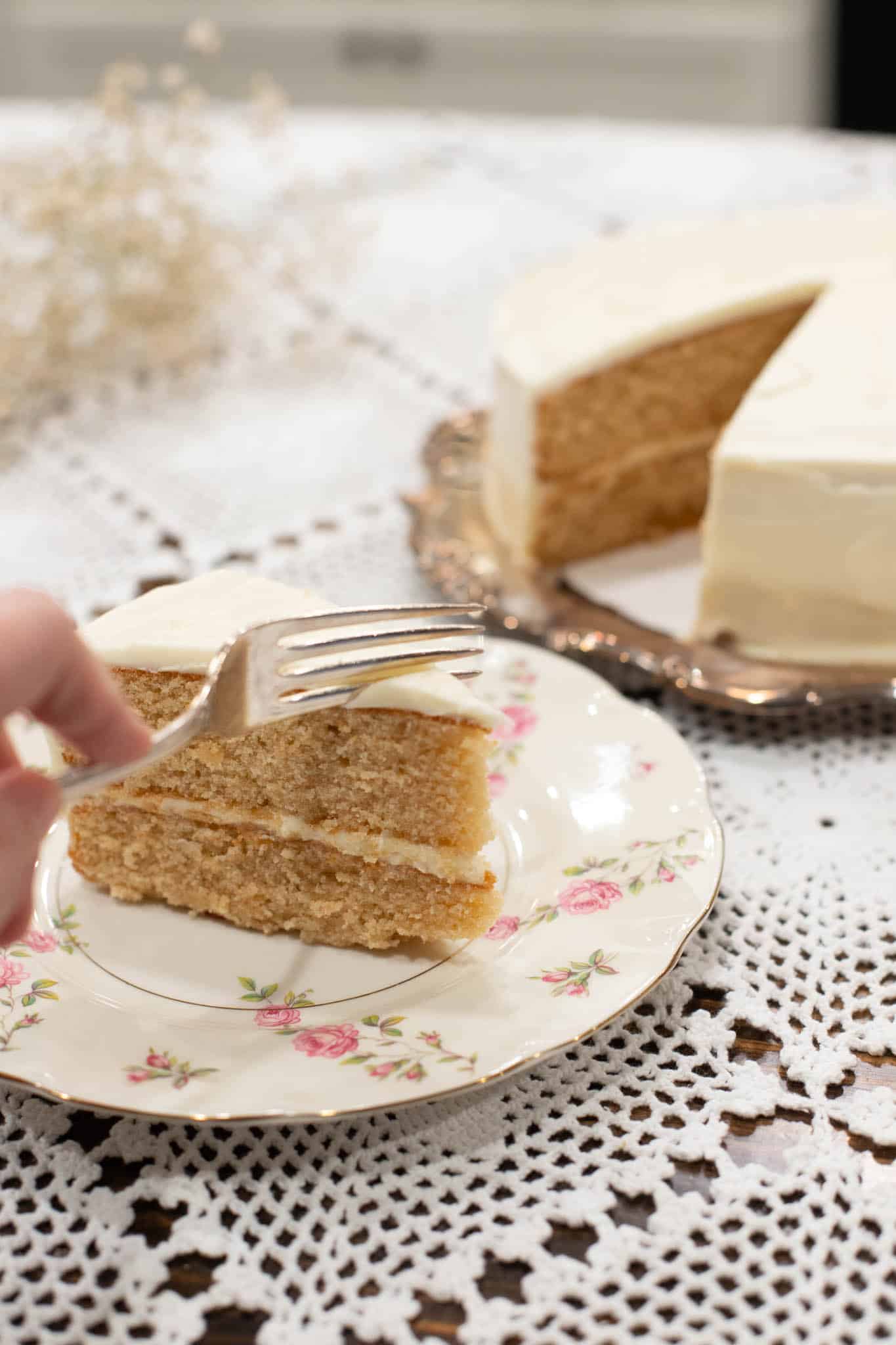 A fork gently pressing into a slice of vanilla cake, ready to take the first bite, with the rest of the cake sitting elegantly in the background.