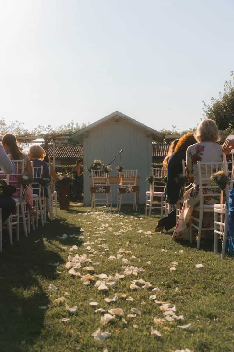 Charming outdoor wedding ceremony in a sunlit garden setting with flower petals and guests.