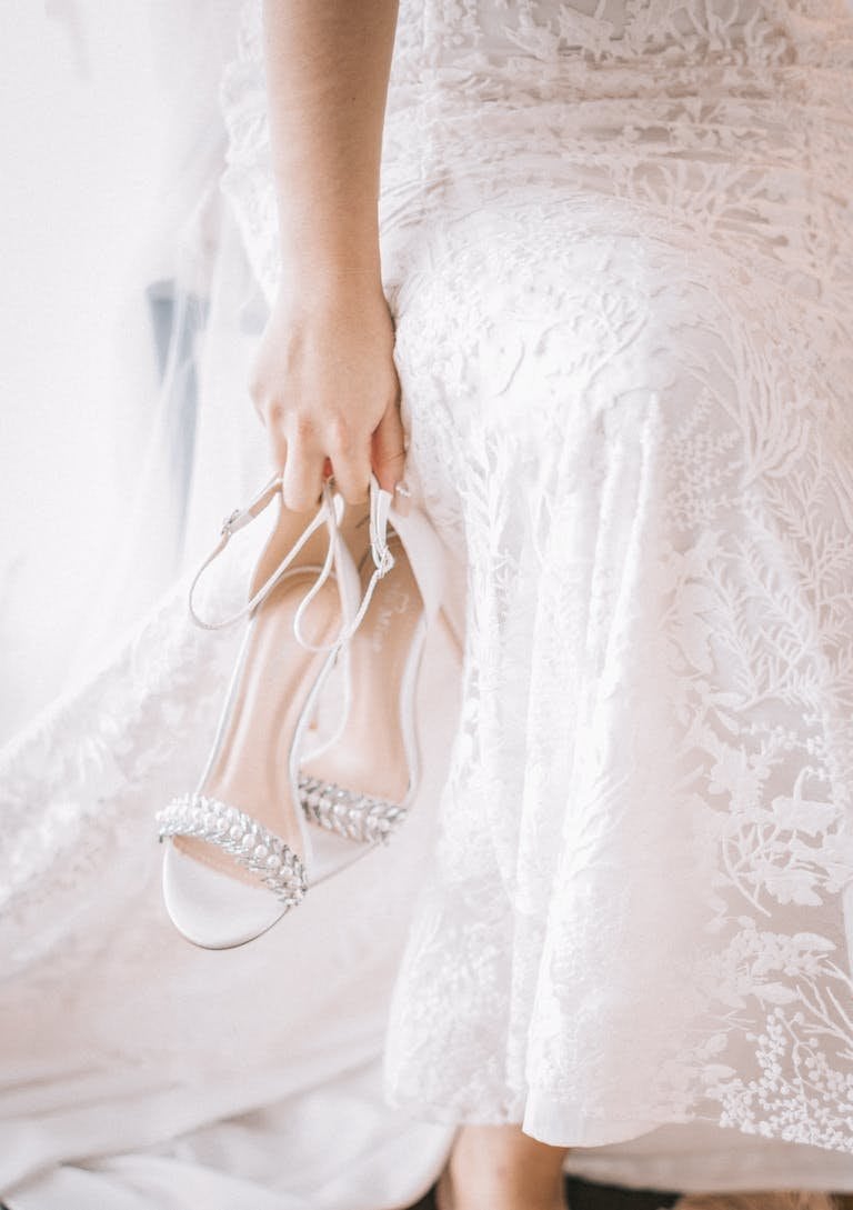 Close-up of woman holding bridal shoes wearing elegant white dress.