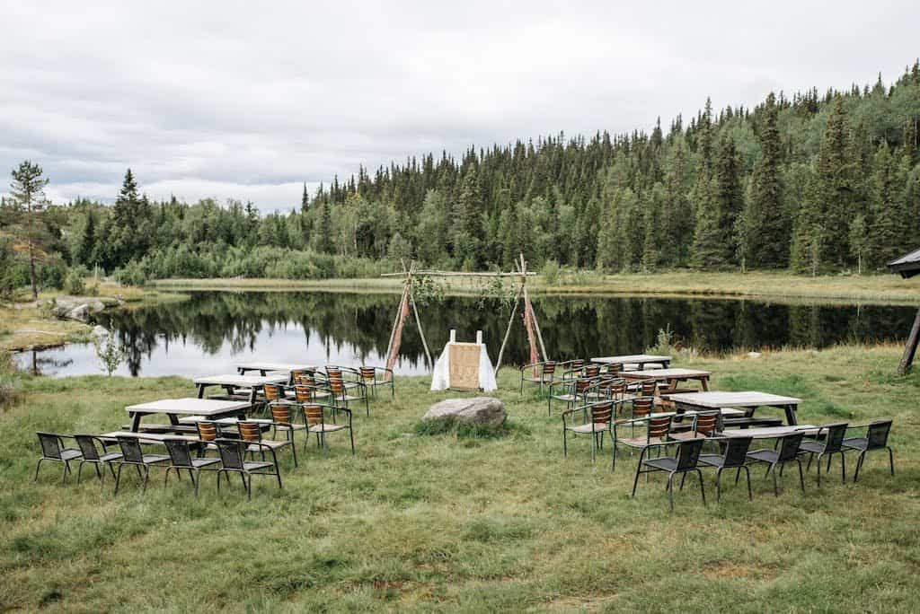 Beautiful outdoor wedding setup by a serene lake surrounded by lush greenery and trees.