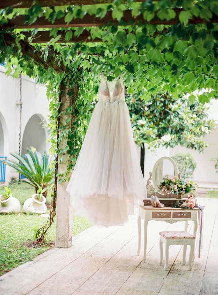 Beautiful wedding dress hanging in a picturesque outdoor garden setup with greenery.