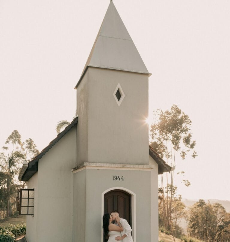 Couple in love embraces by a charming chapel during daylight, evoking romance and tranquility.
