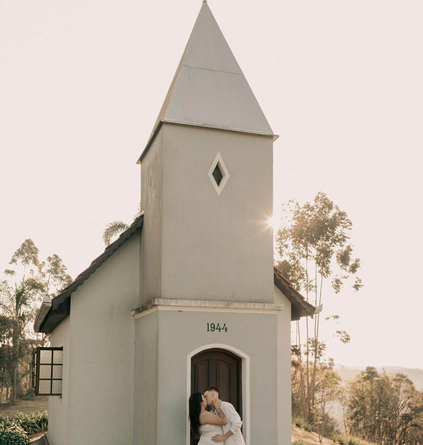 Couple in love embraces by a charming chapel during daylight, evoking romance and tranquility.