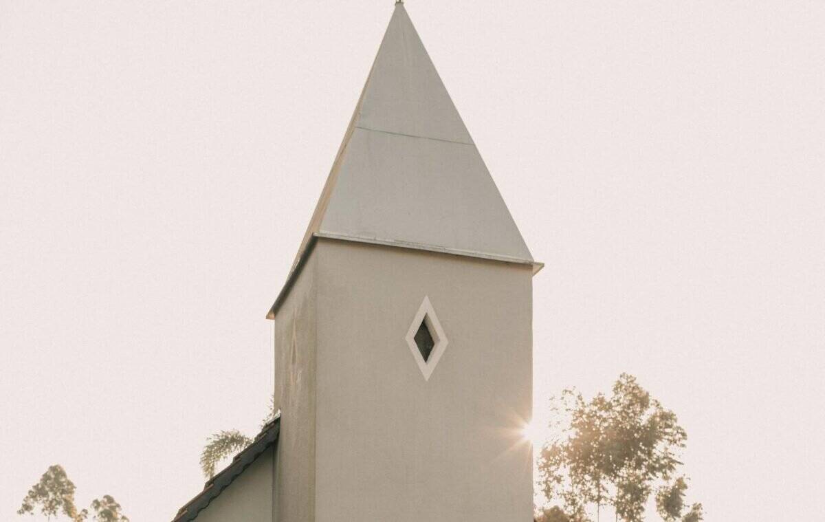 Couple in love embraces by a charming chapel during daylight, evoking romance and tranquility.