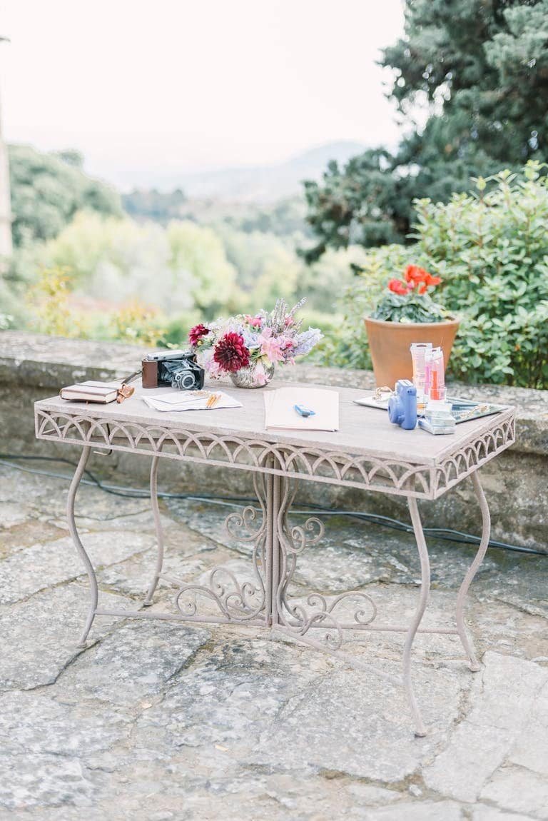Elegant table setup with flowers and vintage camera on a rustic terrace.