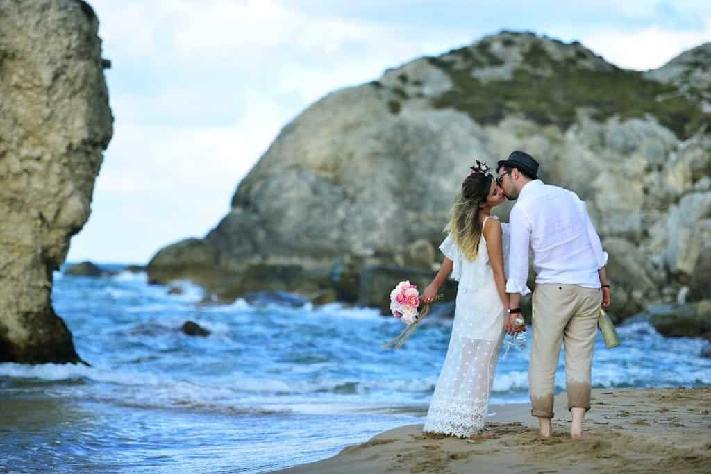 A couple shares a romantic moment on a sandy beach, embracing with a scenic ocean backdrop.