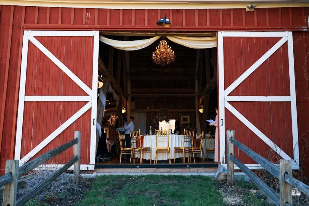 A rustic barn wedding venue with open doors, set for an event with elegant chandeliers and gold chairs.