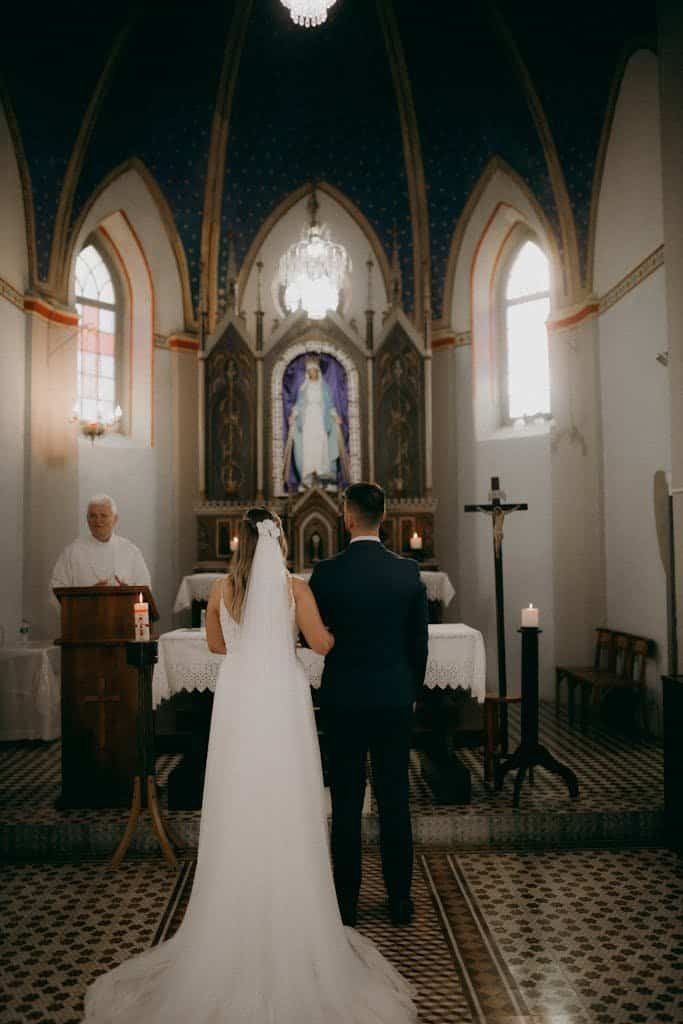 Bride and groom stand before a priest in a beautiful historic church, exchanging vows.