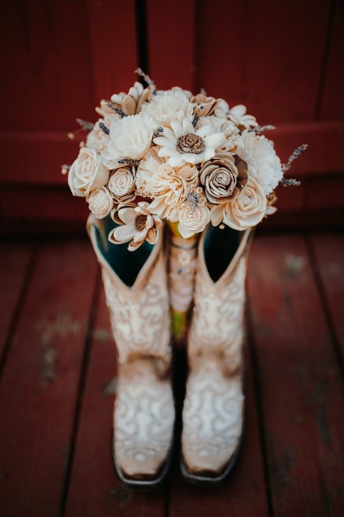 Rustic wedding bouquet with flowers placed in vintage cowboy boots on wooden planks.