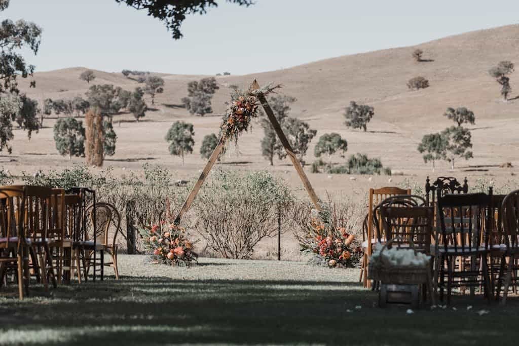 Rustic wedding setup with chairs and floral arch in a picturesque outdoor setting.