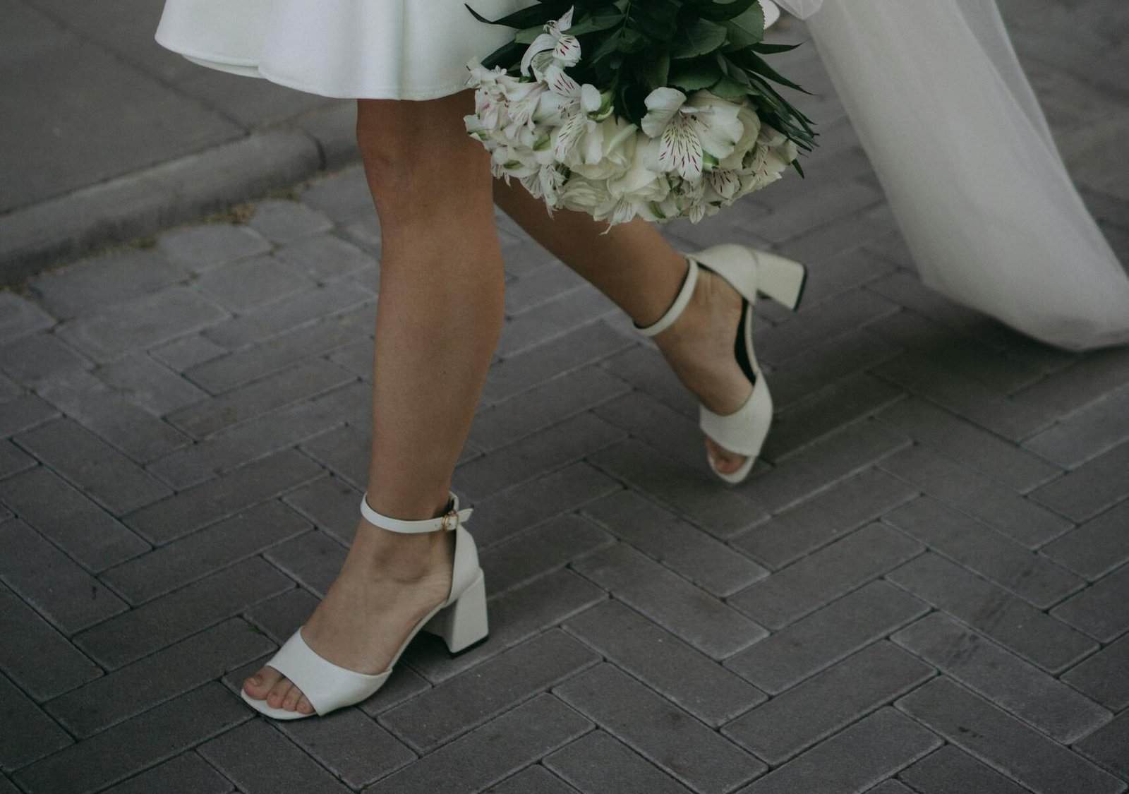 Elegant bride walking with a white bouquet, wearing a short wedding dress and veil.